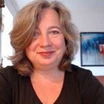 Frances Dahlenburg am Schreibtisch in die Kamera lächelnd.