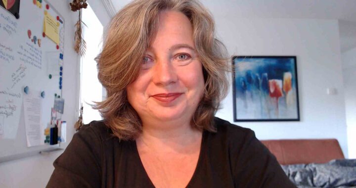 Frances Dahlenburg am Schreibtisch in die Kamera lächelnd.