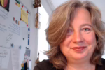 Frances Dahlenburg am Schreibtisch in die Kamera lächelnd.