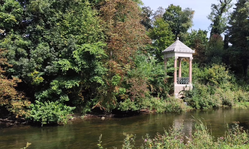 Landschaft mit kleinem Gartenhaus und Fluss in Donaueschingen. Zwischenstopp auf dem Weg zum Kongress in Zürich über Gott, Gewalt und Schuldgefühle der Opfer mit ihren Traumata.