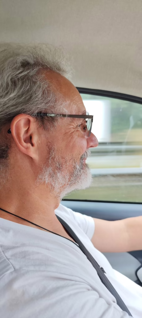 Stephan im weißen T-shirt am Steuer des Autos, lächelnd. Ein sonniger Tag im September 2025