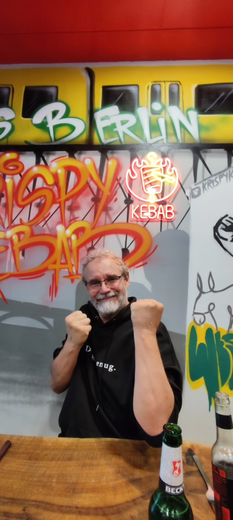 Stephan mit kämpferischer Geste vor bunter Graffity-Wand in einem Lokal.