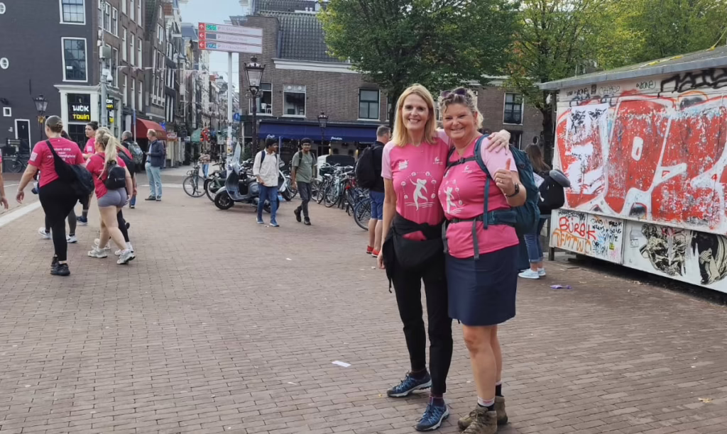 Rosa gekleidete Frauen in einer Fußgängerzone, Lächeln, Umarmung, fröhliche Geste, Sportkleidung. Frauen beim Brustkrebs-Marsch in Amsterdam im September 2025