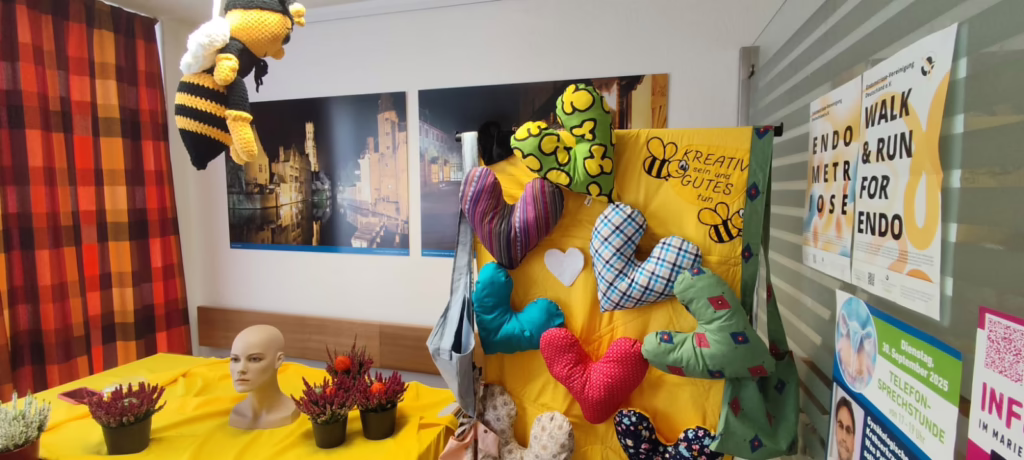 Raum im Marienhospital Wesel, bunt dekoriert mit Herzkissen vor gelber Wand. Zum Brustkrebsinformationstag am 28. September 2025 konnte Frances die Frauen kennenlernen, die ihr Herzkissen genäht hatten, das sie bei der Genesung begleitete.