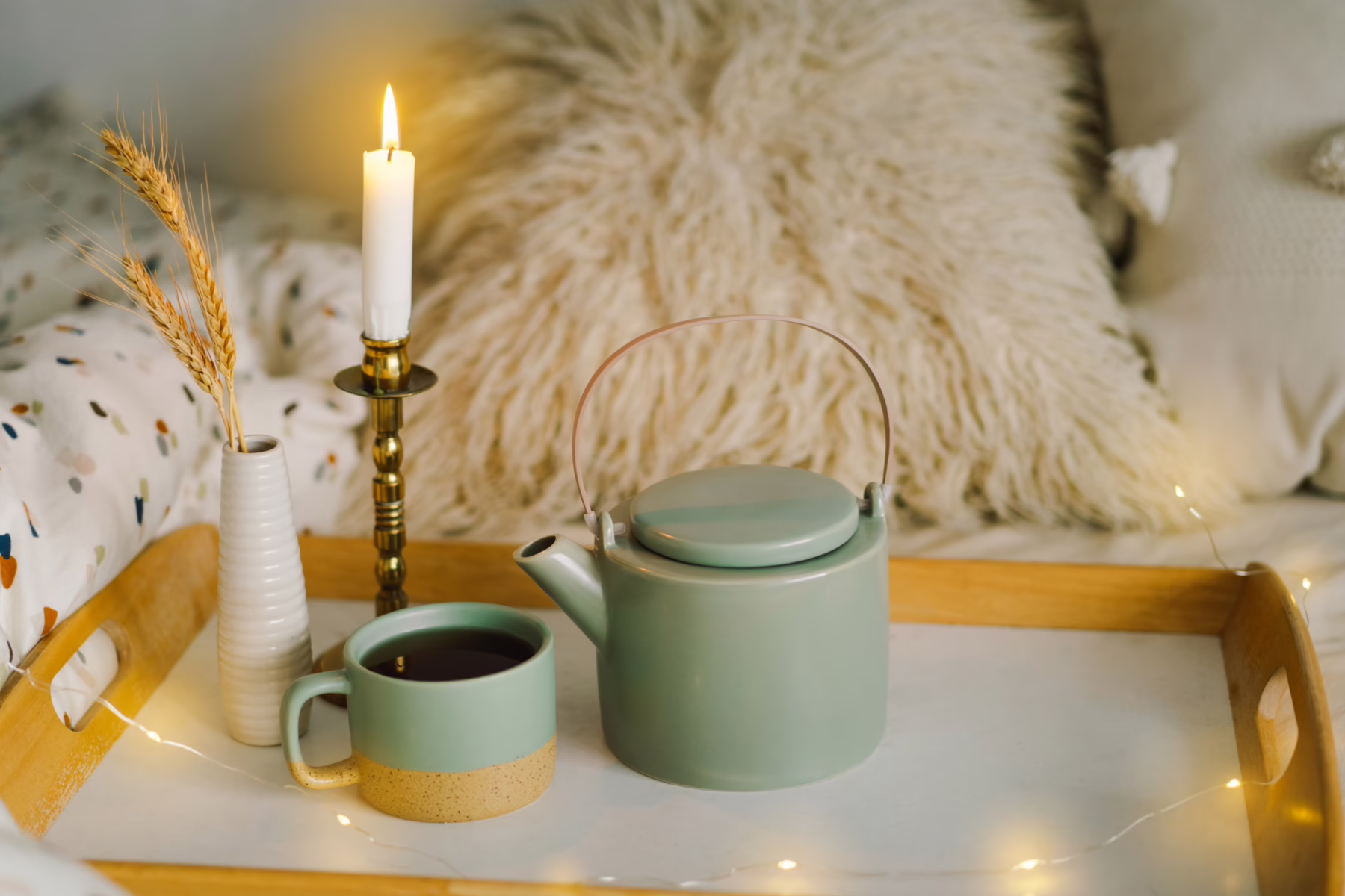 Brennende Wachskerze vor beigefarbener Wolldecke auf einem Tablett mit einer Tasse Kaffee. Der Adventskalender für Menschen mit Geschichte/n lädt zu Ruhe und innerer Einkehr ein.